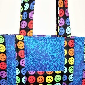 Puede incluir: Un bolso de tela con un dise&ntilde;o de patchwork de tela negra estampada con caras sonrientes de colores y tela azul con un patr&oacute;n animal texturizado. El bolso incluye dos asas de tela a juego con el mismo estampado de caras sonrientes.