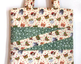 Op de afbeelding: Een gewatteerde draagtas van crèmekleurige stof met een herhalend patroon van katten die diverse accessoires dragen zoals hoge hoeden, baretten en bloemenkransen, geaccentueerd door twee diagonale banen van groene stof met witte bloemen.