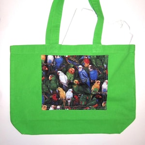 May include: A bright lime green tote bag featuring a rectangular center panel with a dense, colorful print of various parrots and parakeets perched among dark green foliage. The bag has two matching lime green fabric shoulder straps.