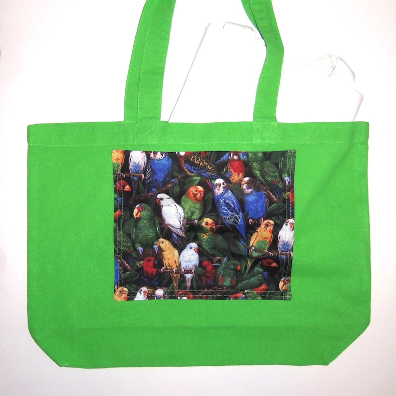 May include: A bright lime green tote bag featuring a rectangular center panel with a dense, colorful print of various parrots and parakeets perched among dark green foliage. The bag has two matching lime green fabric shoulder straps.