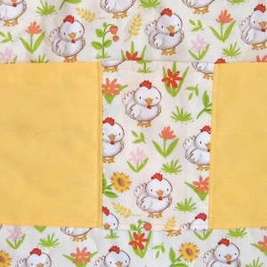May include: A quilted fabric item featuring a repeating pattern of white chickens with red combs, green grass, and orange and yellow flowers. A solid yellow horizontal band spans the center, dividing the patterned fabric into three sections.