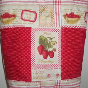 May include: A quilted fabric cover featuring a patchwork design with red and white patterns. The centre panel displays a strawberry illustration with the text "Fraise" and "Strawberry" above a recipe block. Other sections show bowls of strawberries.