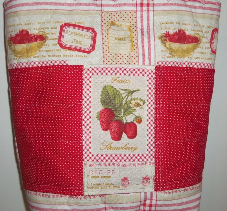 May include: A quilted fabric cover featuring a patchwork design with red and white patterns. The centre panel displays a strawberry illustration with the text "Fraise" and "Strawberry" above a recipe block. Other sections show bowls of strawberries.