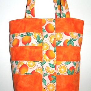 May include: A quilted tote bag with a vibrant orange and white citrus fruit pattern. The bag features solid orange panels and handles, with a repeating design of oranges and orange slices on a white background. The bag is designed for carrying items.