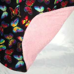 May include: A black and white fabric with a colorful butterfly pattern. The fabric is folded in half, revealing a pink fleece lining.