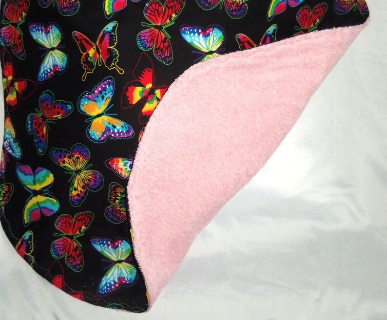 May include: A black and white fabric with a colorful butterfly pattern. The fabric is folded in half, revealing a pink fleece lining.