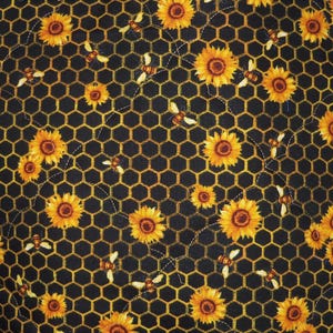 May include: A fabric featuring a repeating pattern of yellow sunflowers and small bees scattered across a black background with a yellow honeycomb grid. The material has visible white stitching lines that create a quilted texture throughout.