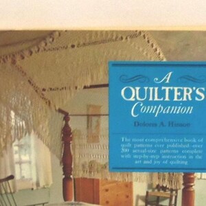 Puede incluir: Un libro titulado A Quilter's Companion de Doloris A. Hinson con una superposici&oacute;n rectangular azul y texto blanco. La portada muestra una cama con dosel con un dosel de ganchillo blanco y flecos en una habitaci&oacute;n con muebles de madera.