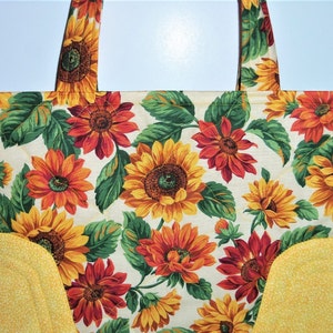 May include: A yellow and white quilted tote bag with a sunflower and fall leaf print. The bag has two yellow fabric handles.