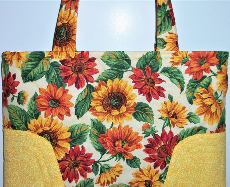 May include: A yellow and white quilted tote bag with a sunflower and fall leaf print. The bag has two yellow fabric handles.