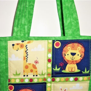 May include: A quilted tote bag featuring a vibrant green fabric border and handles. The central panel displays a patchwork design with cartoon illustrations of a yellow giraffe on a light background and a lion on a dark blue background.