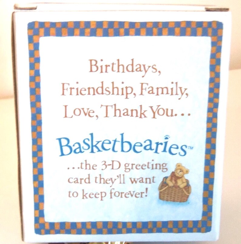 May include: A white box with a blue and orange checkered border. The text reads "Birthdays, Friendship, Family, Love, Thank You..." and "Basketbearies" with a small illustration of a teddy bear in a basket. The text continues, "...the 3-D greeting card they'll want to keep forever!"