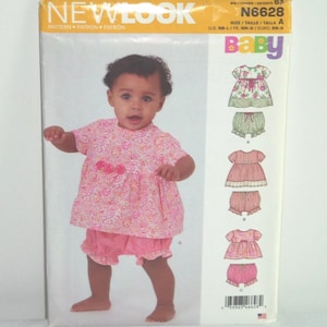 May include: A baby wearing a pink floral print outfit, including a top and shorts. The image is on a New Look pattern envelope, with the word "Baby" in colorful letters. The pattern number is N6628.