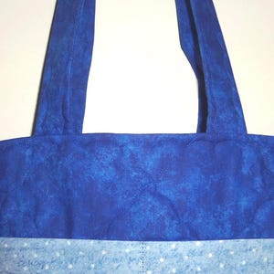 May include: A quilted tote bag featuring a deep royal blue upper section with a mottled texture and a lighter sky blue lower section adorned with a white polka dot pattern. The bag includes two matching royal blue fabric shoulder straps.