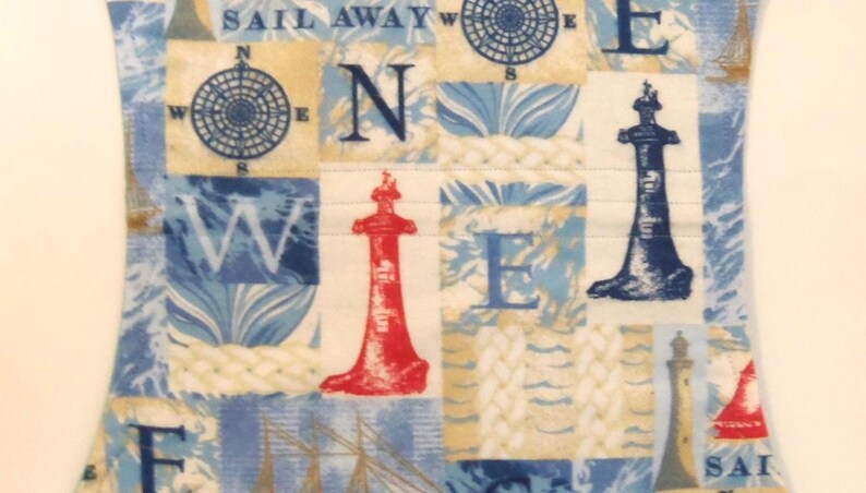 May include: A nautical-themed fabric with a patchwork design. The design features compasses, lighthouses, and the words "SAIL AWAY" and "W E". The color palette includes shades of blue, beige, and red.