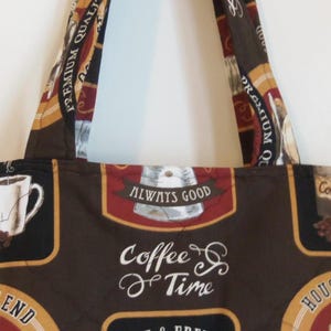 Puede incluir: Un bolso de tela con un estampado de caf&eacute; en tonos marr&oacute;n, negro y crema. El dise&ntilde;o incluye ilustraciones de tazas de caf&eacute;, granos y textos que dicen "Premium Quality", "Always Good", "Coffee Time" y "House Blend" por toda la superficie.