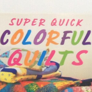 May include: A book titled SUPER QUICK COLORFUL QUILTS with a cover featuring a stack of folded fabric quilts in various patterns and bright colors including blue, yellow, red, and green. The text is printed in large, multi-colored sans-serif letters.