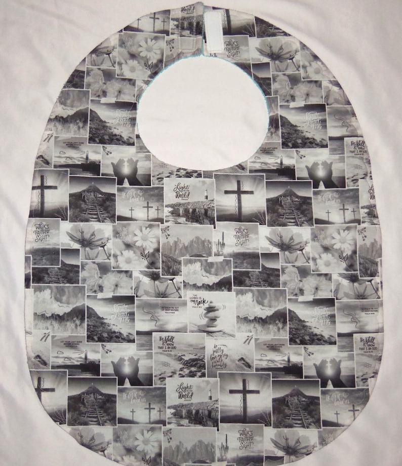 May include: A bib featuring a black and white collage print of various religious and nature-themed images, including crosses, mountains, flowers, and stacked stones. The fabric has a rounded shape with a central neck opening and a hook-and-loop closure.