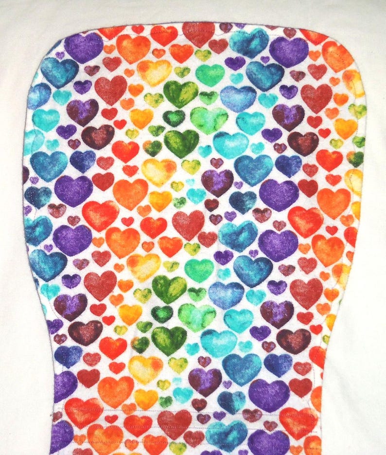 May include: A white fabric item covered in a pattern of colorful hearts in shades of red, orange, yellow, green, blue, and purple. The hearts are of varying sizes and are densely packed together.