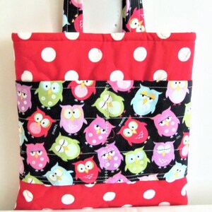 May include: A quilted tote bag featuring a red fabric with large white polka dots on the top and bottom sections. The centre panel is black fabric decorated with a colourful pattern of cartoon owls in shades of pink, green, blue, and yellow.