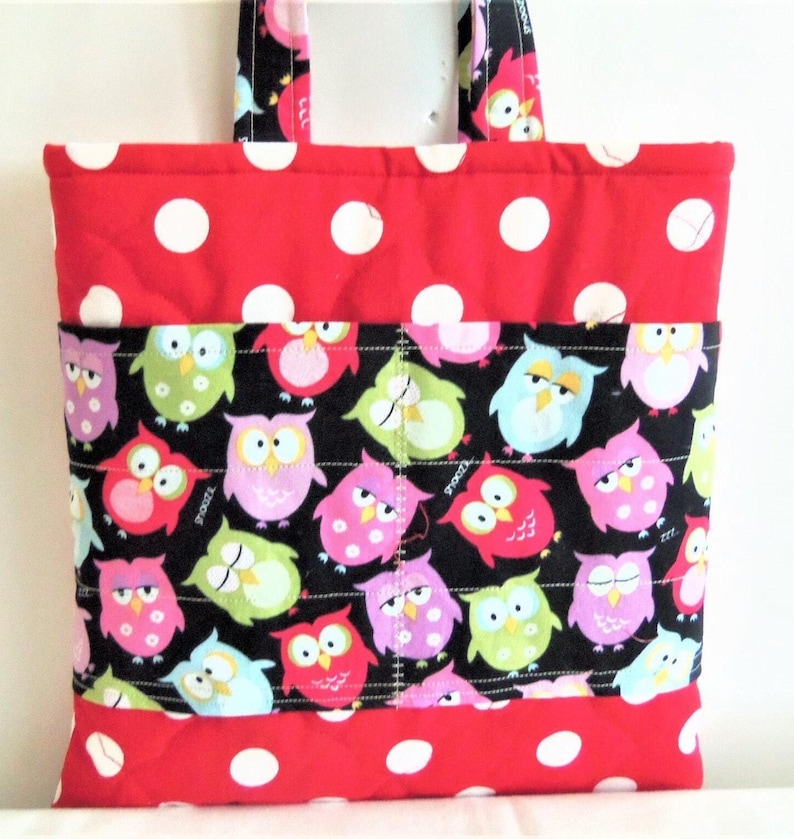 May include: A quilted tote bag featuring a red fabric with large white polka dots on the top and bottom sections. The centre panel is black fabric decorated with a colourful pattern of cartoon owls in shades of pink, green, blue, and yellow.