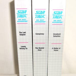 May include: Three white VHS tape cases for Star Trek The Next Generation, each featuring a grid pattern, teal and pink text, and episode titles including The Last Outpost, Lonely Among Us, Conspiracy, The Neutral Zone, Unnatural Selection, and A Matter of Honor.