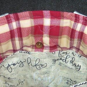 May include: A red and cream plaid fabric tote bag with a cream lining. The lining has the text "enjoy life with family for a good day" printed on it.