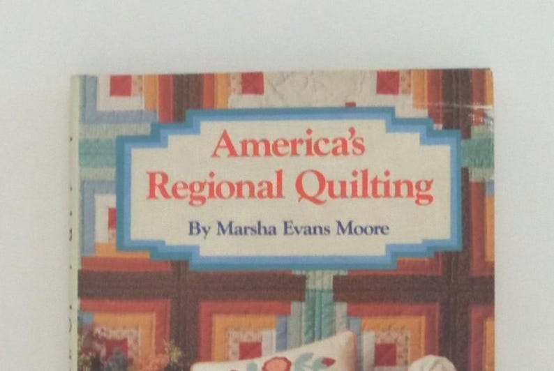 May include: A book titled America's Regional Quilting by Marsha Evans Moore. The cover features a colorful geometric quilt pattern in shades of red, orange, yellow, and blue, with the title printed in red text inside a light blue rectangular frame.