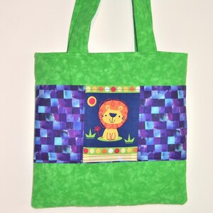 May include: A quilted green tote bag featuring two long handles and a central horizontal panel. The panel displays a dark blue section with a cartoon lion illustration, flanked by two sections of a purple and blue checkered pattern fabric.