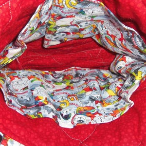 May include: A quilted fabric bag interior featuring a bright red lining with a subtle tonal dot pattern. The interior pockets are lined with a white fabric printed with a colorful, repeating pattern of stylized cats in various poses.