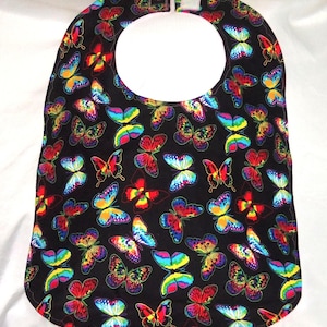 May include: A black bib with a colorful butterfly pattern. The bib has a white neck opening and a velcro closure.