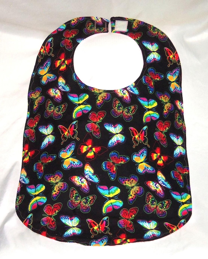 May include: A black bib with a colorful butterfly pattern. The bib has a white neck opening and a velcro closure.