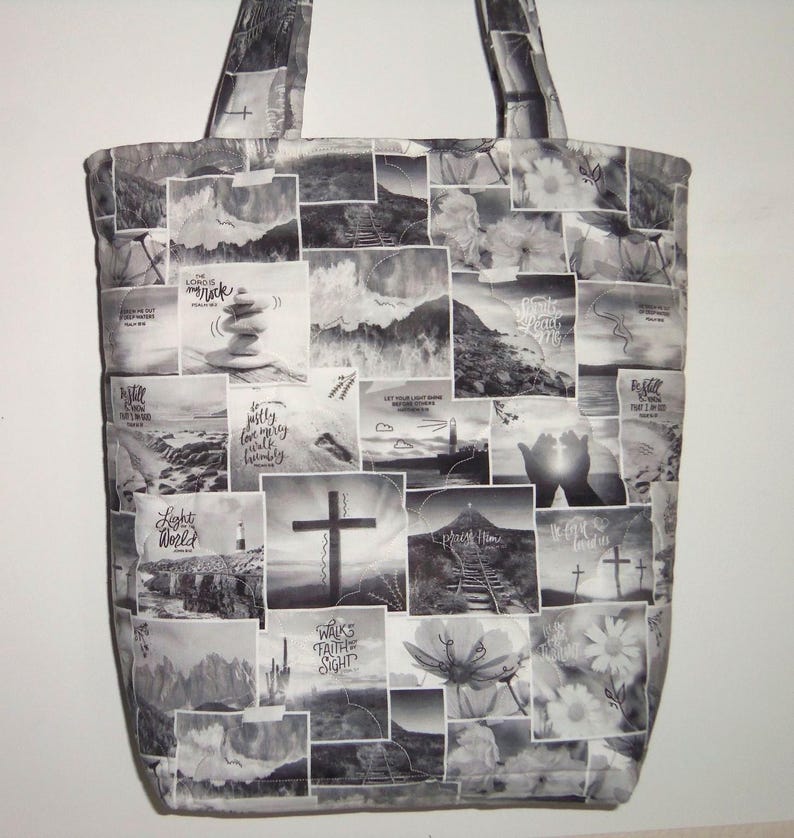 May include: Black and white tote bag with a patchwork design featuring religious imagery. The bag displays images of crosses, landscapes, and inspirational text. It has two handles for carrying.