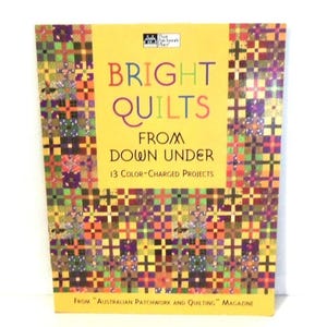 May include: A softcover book titled Bright Quilts From Down Under: 13 Color-Charged Projects From Australian Patchwork and Quilting Magazine. The cover features a yellow center with multicolored patchwork quilt patterns on the sides and bottom.