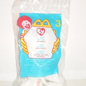 May include: A sealed clear plastic bag containing a Ty Flip the Cat toy. The packaging features a light blue background, a yellow McDonald's arch logo, the number 3, and an illustration of Ronald McDonald. Text includes Flip the Cat Toy Animal.