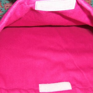 May include: A pet bed with a bright pink interior and a teal exterior patterned with cartoon animals. The bed has a rectangular shape with a soft, plush texture. White velcro closures are visible.
