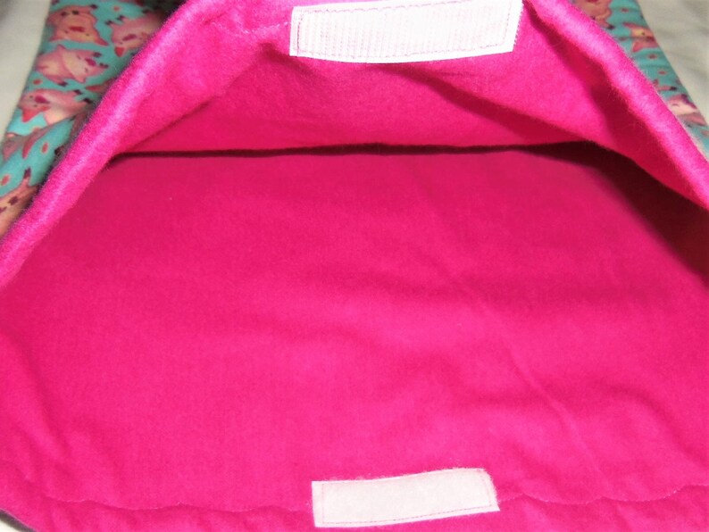 May include: A pet bed with a bright pink interior and a teal exterior patterned with cartoon animals. The bed has a rectangular shape with a soft, plush texture. White velcro closures are visible.