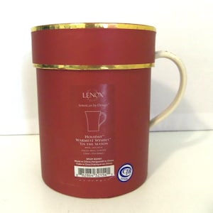 May include: A cylindrical red Lenox gift box with a gold rim and a white handle protruding from the side. The label features the text Lenox, American by Design, Holiday Warmest Wishes, Tis the Season, and a 12 oz / 354.84 ml capacity.