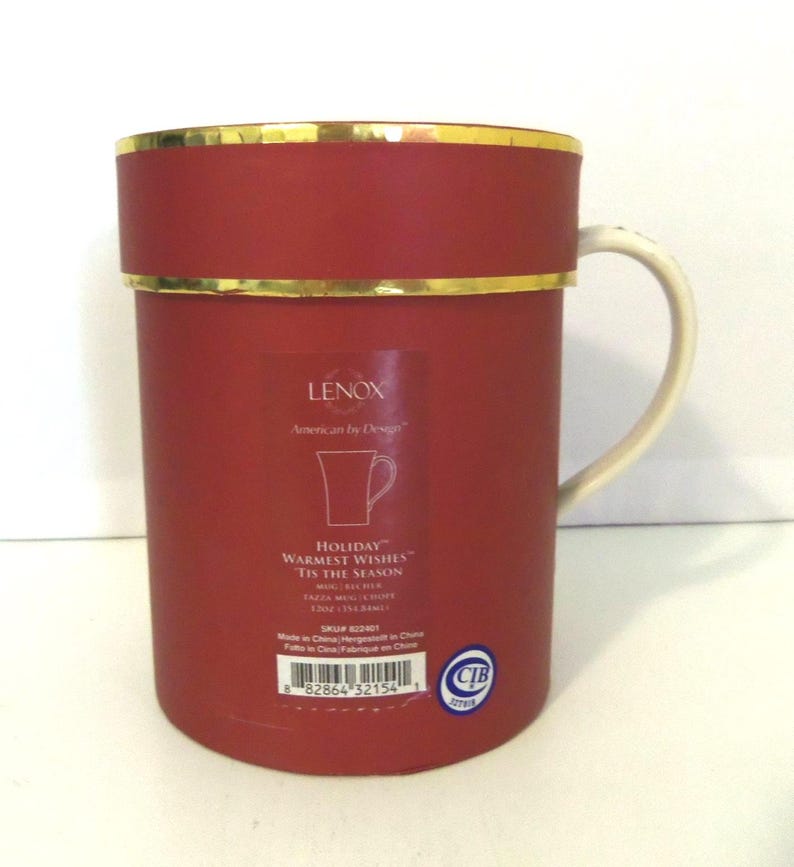 May include: A cylindrical red Lenox gift box with a gold rim and a white handle protruding from the side. The label features the text Lenox, American by Design, Holiday Warmest Wishes, Tis the Season, and a 12 oz / 354.84 ml capacity.
