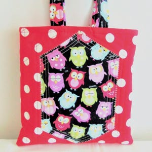 May include: A square fabric tote bag featuring a bright red background with white polka dots. The centre panel is a black fabric patch with a repeating pattern of colourful owls in shades of pink, lime green, and light blue, finished with white stitching.