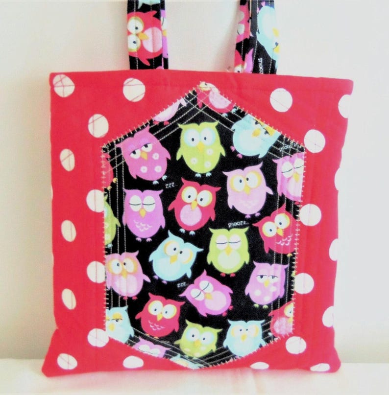 May include: A square fabric tote bag featuring a bright red background with white polka dots. The centre panel is a black fabric patch with a repeating pattern of colourful owls in shades of pink, lime green, and light blue, finished with white stitching.
