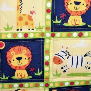 May include: A quilted fabric panel featuring a repeating pattern of cartoon animals including giraffes, lions, and zebras. The design is divided into squares by a lime green border with colorful polka dots, set against cream and navy blue backgrounds.