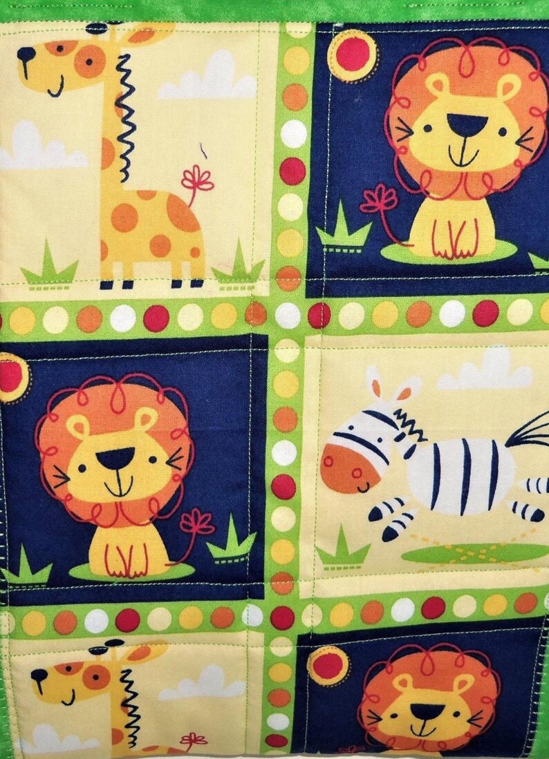 May include: A quilted fabric panel featuring a repeating pattern of cartoon animals including giraffes, lions, and zebras. The design is divided into squares by a lime green border with colorful polka dots, set against cream and navy blue backgrounds.