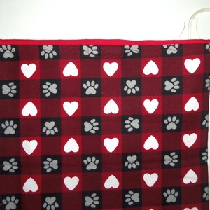 May include: Red and white checkered fabric with a pattern of paw prints and hearts. The fabric has a red border.
