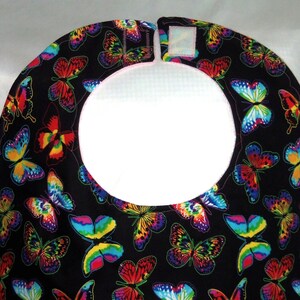 May include: A black bib with a white, round opening and a colorful butterfly pattern. The bib has a white velcro closure.