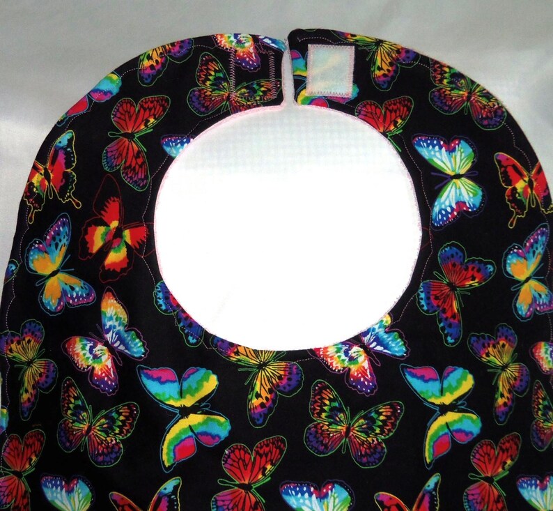 May include: A black bib with a white, round opening and a colorful butterfly pattern. The bib has a white velcro closure.