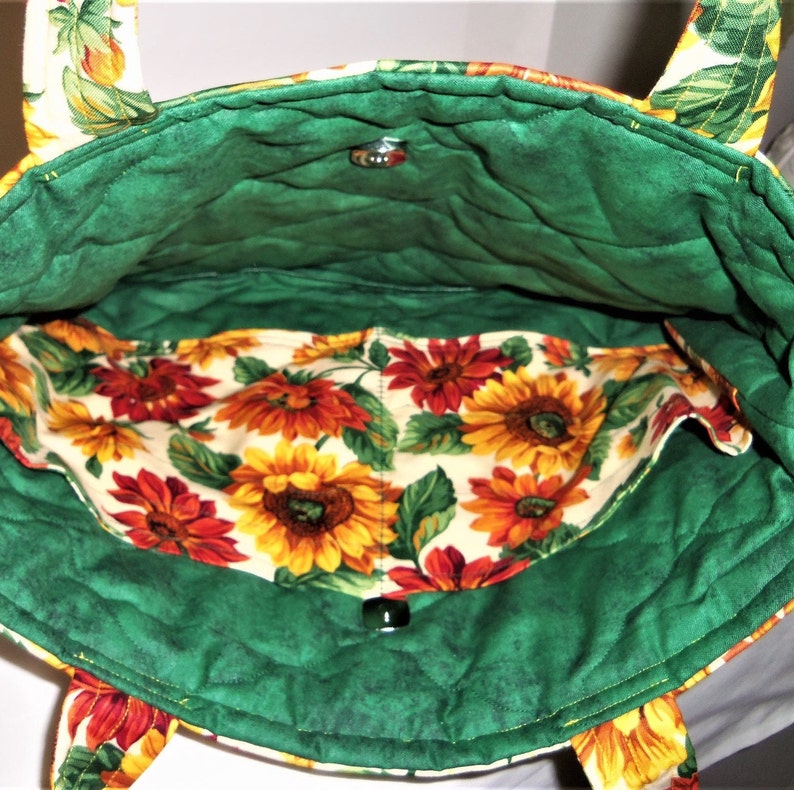 May include: Green quilted tote bag with sunflower print lining. The bag has two straps and a snap closure.
