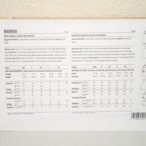 May include: A white Butterick sewing pattern envelope labeled B6905 for baby overalls, a dress, and panties. The back of the envelope displays technical illustrations of the garments, lists suggested fabrics, notions, and detailed sizing charts.