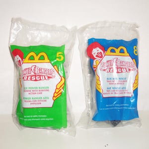 以下が含まれることがあります： Power Rangers Rescueのブランドロゴが入った、未開封のMcDonald'sハッピーセット用プラスチックバッグ2点。左側のバッグは緑色で数字の5が、右側のバッグは青色で数字の8が印刷されています。両方のバッグにMcDonald'sのロゴと玩具の説明が記載されています。