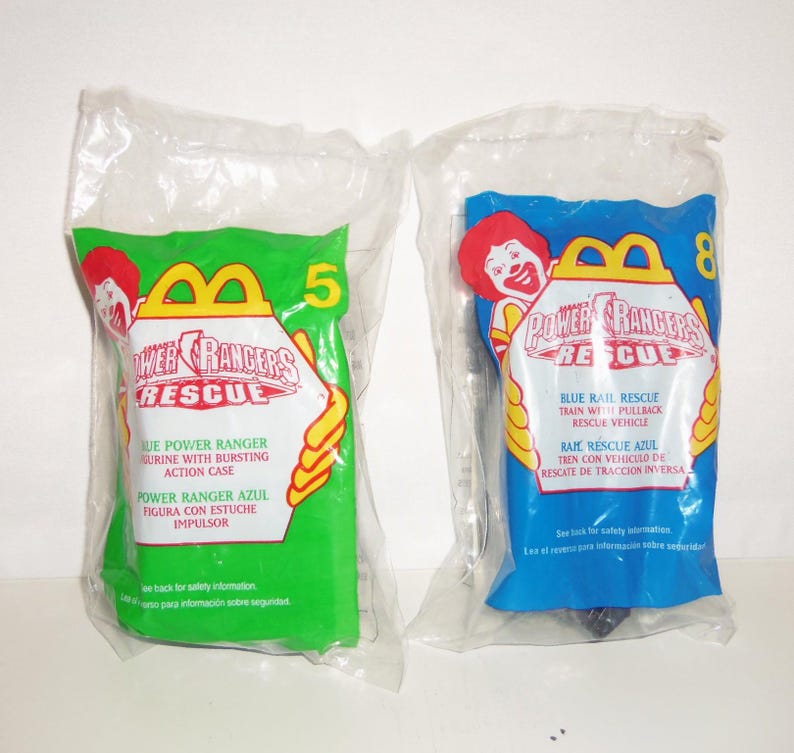 以下が含まれることがあります： Power Rangers Rescueのブランドロゴが入った、未開封のMcDonald'sハッピーセット用プラスチックバッグ2点。左側のバッグは緑色で数字の5が、右側のバッグは青色で数字の8が印刷されています。両方のバッグにMcDonald'sのロゴと玩具の説明が記載されています。